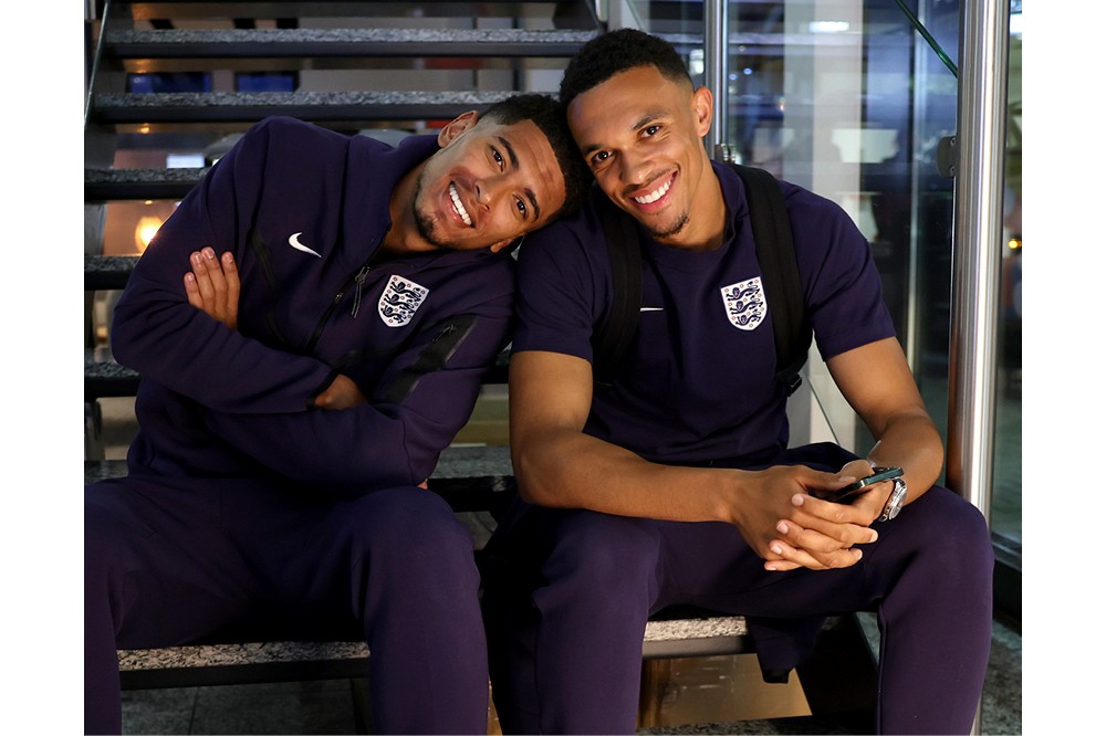 Two men in England training kits sitting on stairs smiling together.